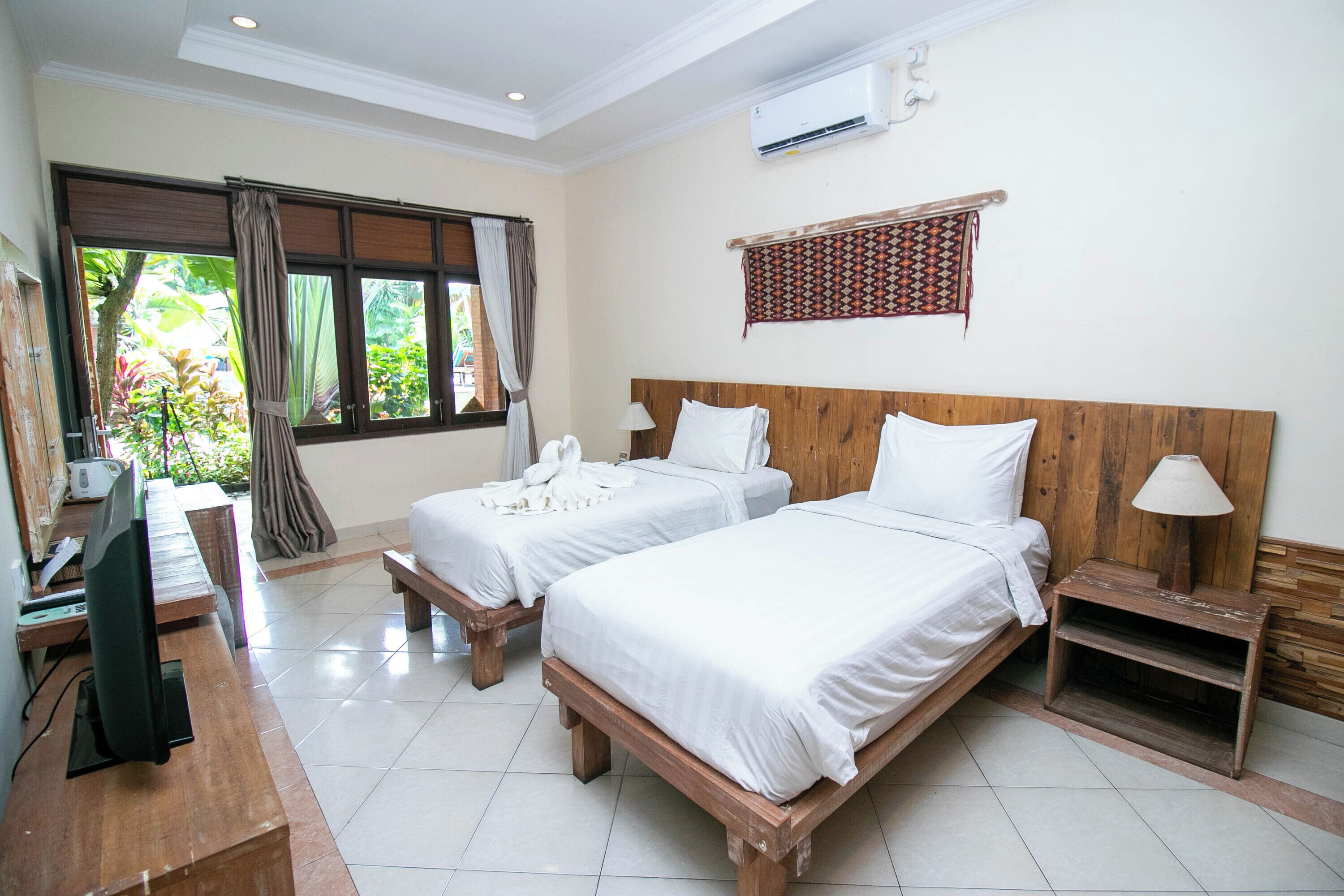 A hotel room with two beds, a desk, a TV, and a window with curtains.