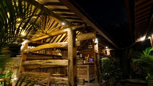 A rustic reception area with a wooden structure, bookshelves, and a reception desk. - Mina Pelasa Hotel and Resto (Legian)