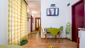 A room with a dining table, chairs, a TV mounted on the wall, and a green curtain. - Apartments Aja and Stefy (Rovinj)
