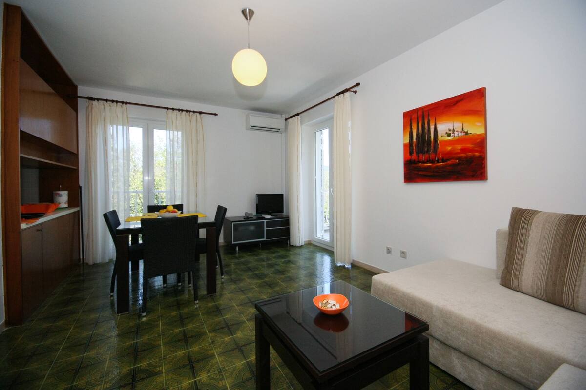 Ein Wohnzimmer mit einer Couch, einem Esstisch mit Stühlen, einem Fernseher und einem Bild an der Wand.
