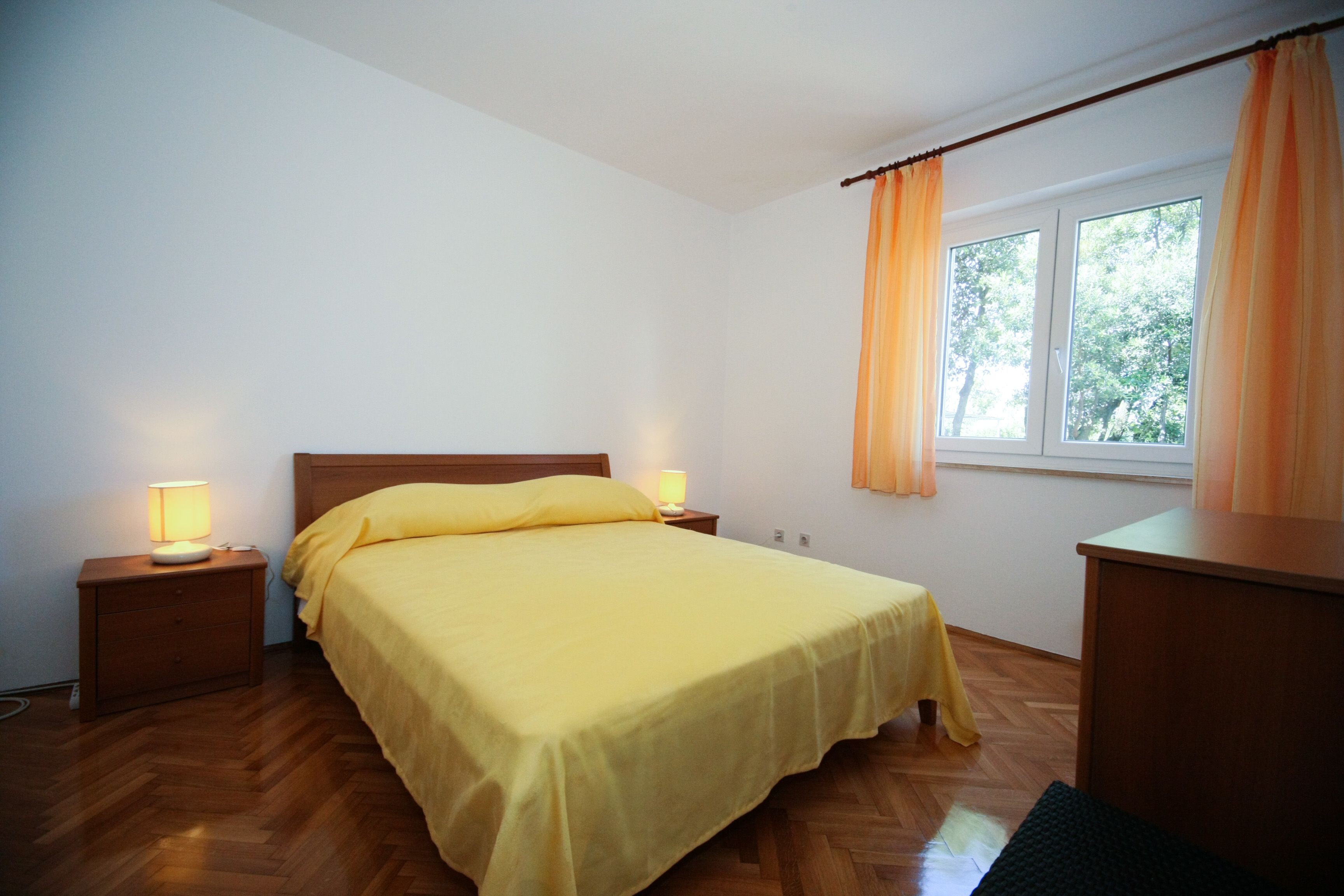 Un dormitorio con cama, mesitas de noche, un escritorio y una ventana con cortinas.