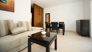 Een moderne woonkamer met een bank, een glazen salontafel, een eethoek met een tafel en stoelen, en een kast.
