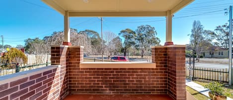 Un espacio al aire libre cubierto, con pared de ladrillo y suelo rojo, con vista a una calle con árboles y un automóvil estacionado.