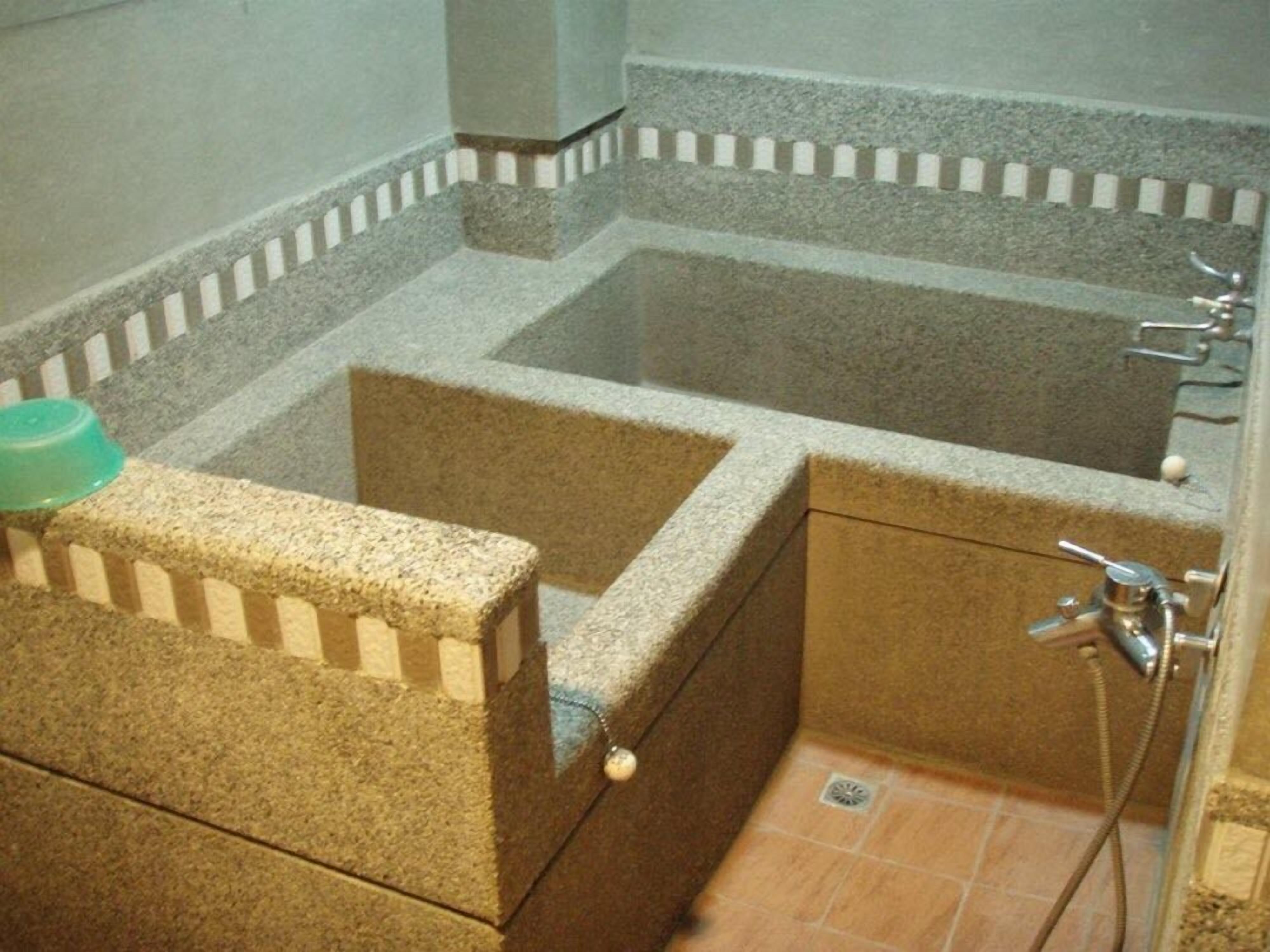 A bathroom with a rectangular bathtub, a shower area, and a green basin on the left.