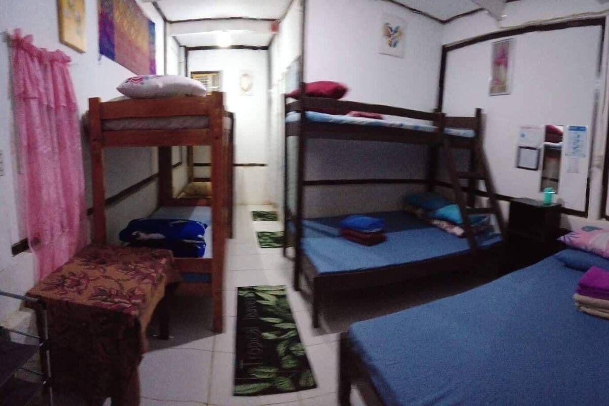 Um dormitório com beliches, uma mesinha e uma cama com almofadas.