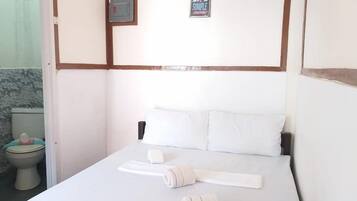 A hotel room with a bed, white linens, a small bedside table, and a wall with a life sign and a picture frame.