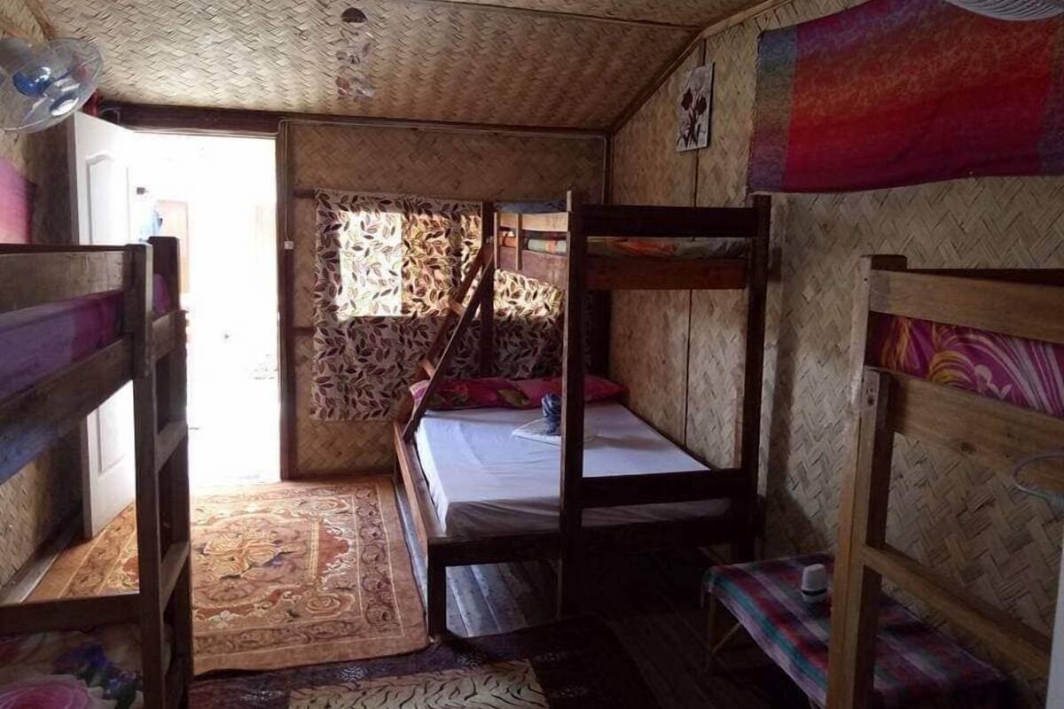 Quarto com beliches, um ventilador, tapete estampado e uma porta que dá para o exterior.