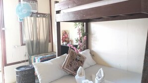 A room with a bunk bed, a bedside table with a picture frame, a fan, and a small trash bin. - Sun Valley Inn - Hostel (El Nido)