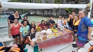 A group of people on a boat with a table of food in front of a rocky cliff. - Sun Valley Inn - Hostel (El Nido)