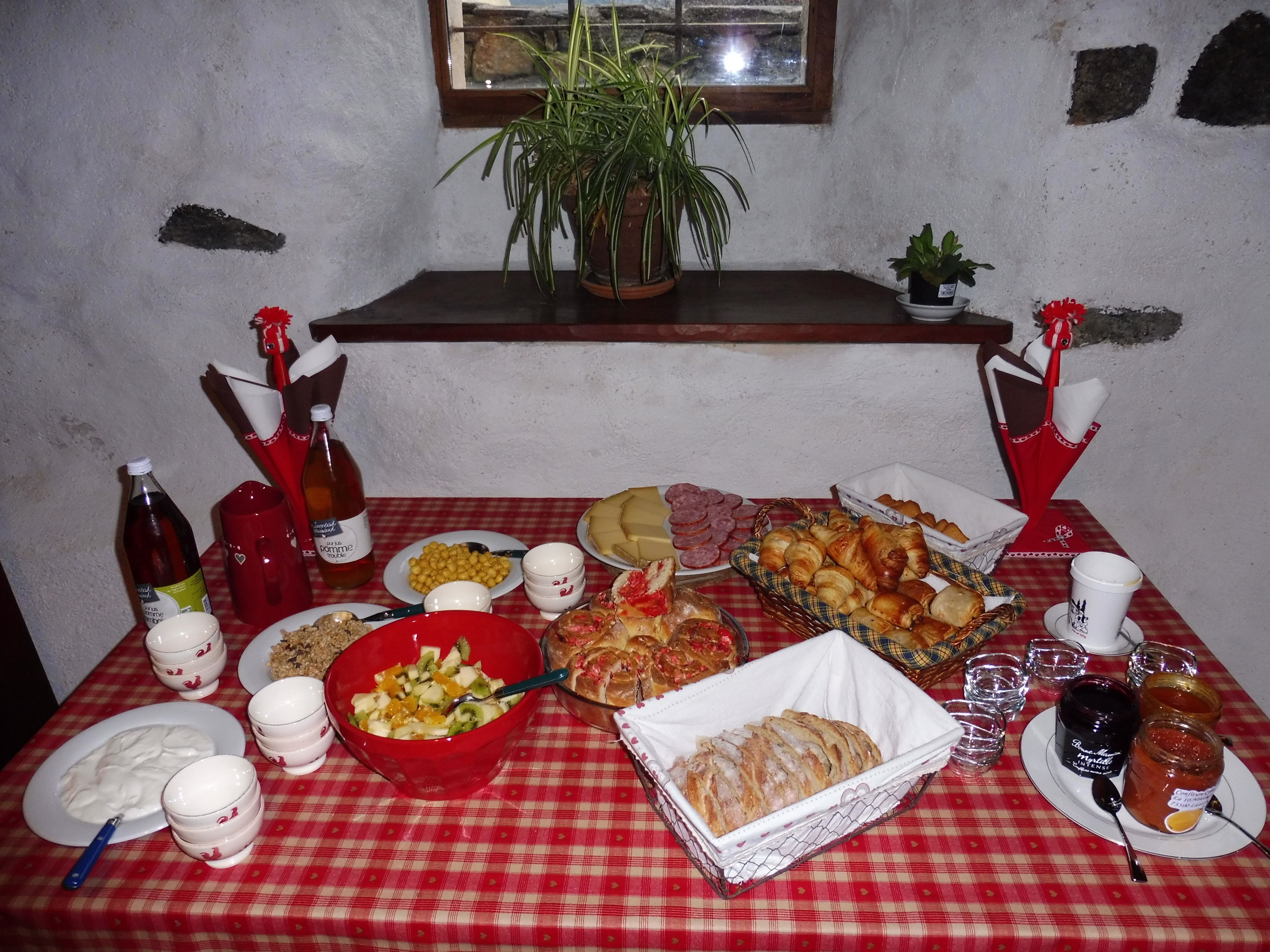 Une table dressée avec divers aliments, notamment du pain, des pâtisseries et une salade de fruits, ainsi que plusieurs bouteilles et tasses.