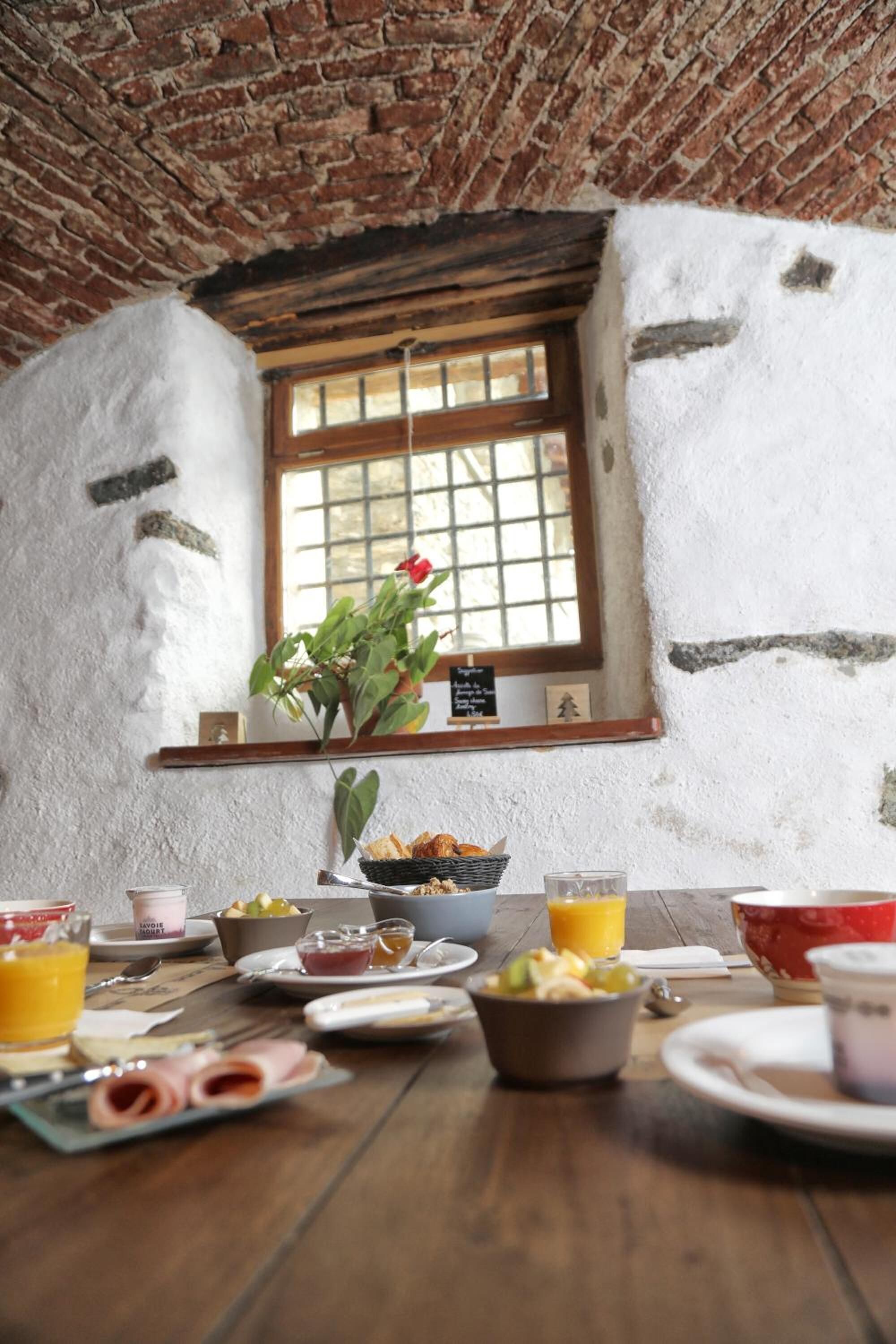 A rustic breakfast table with various breakfast items, a window with a view, and a brick ceiling.
