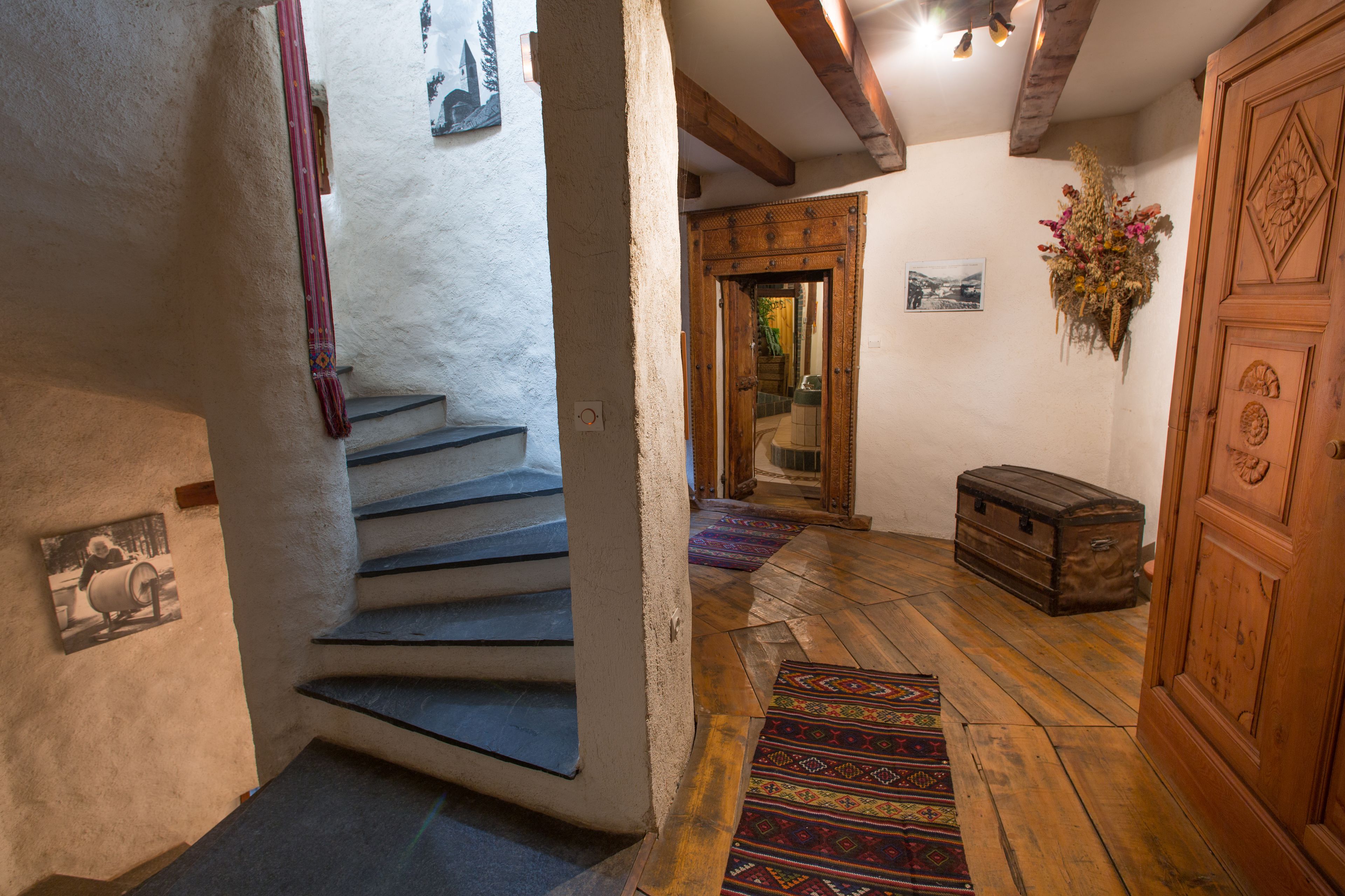 Eine Treppe führt zu einem Raum mit einer Holzkiste, einem gemusterten Teppich und einem an der Wand hängenden Bild.
