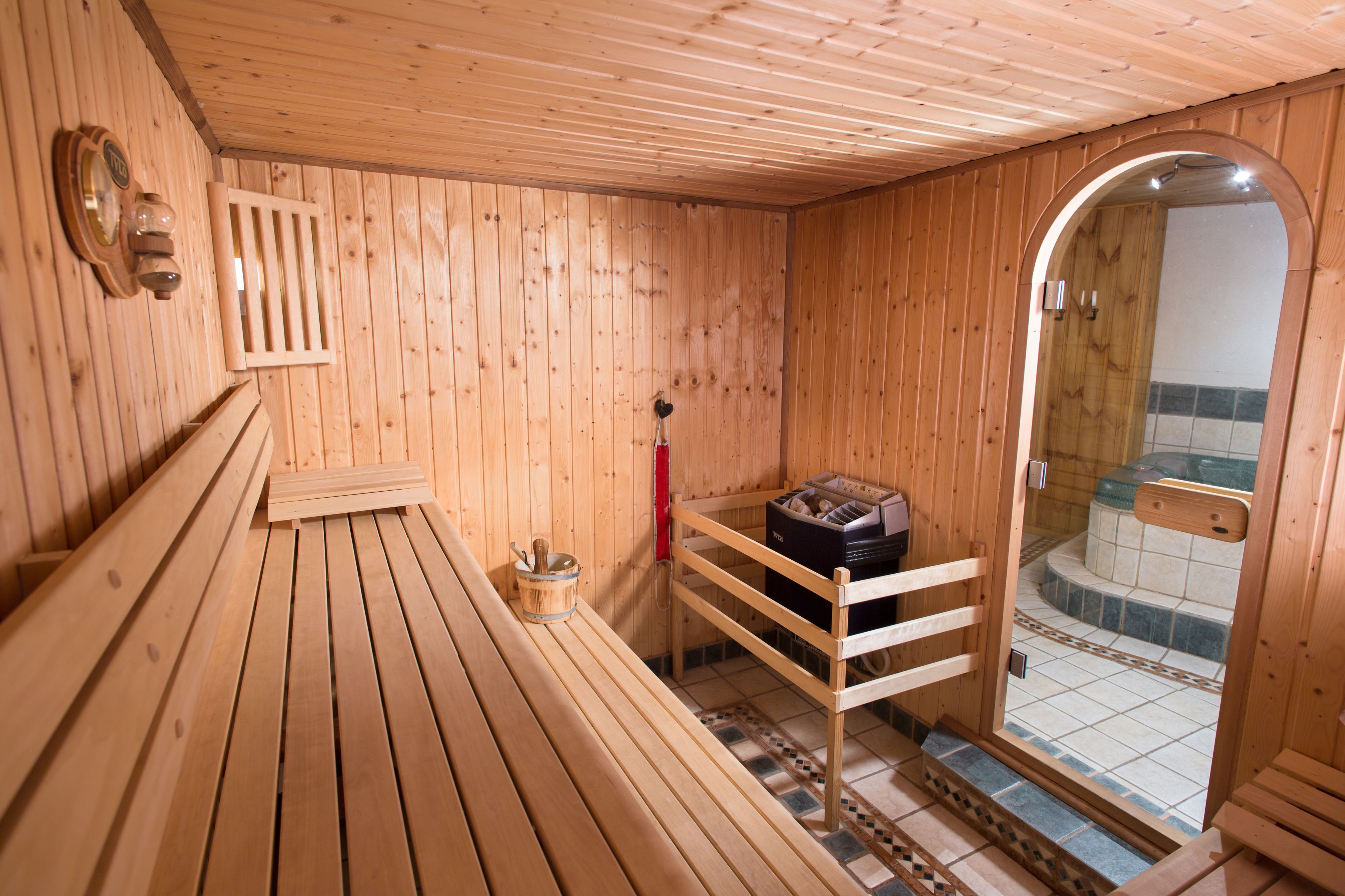 A wooden sauna room with benches, a sauna heater, and a tiled floor.