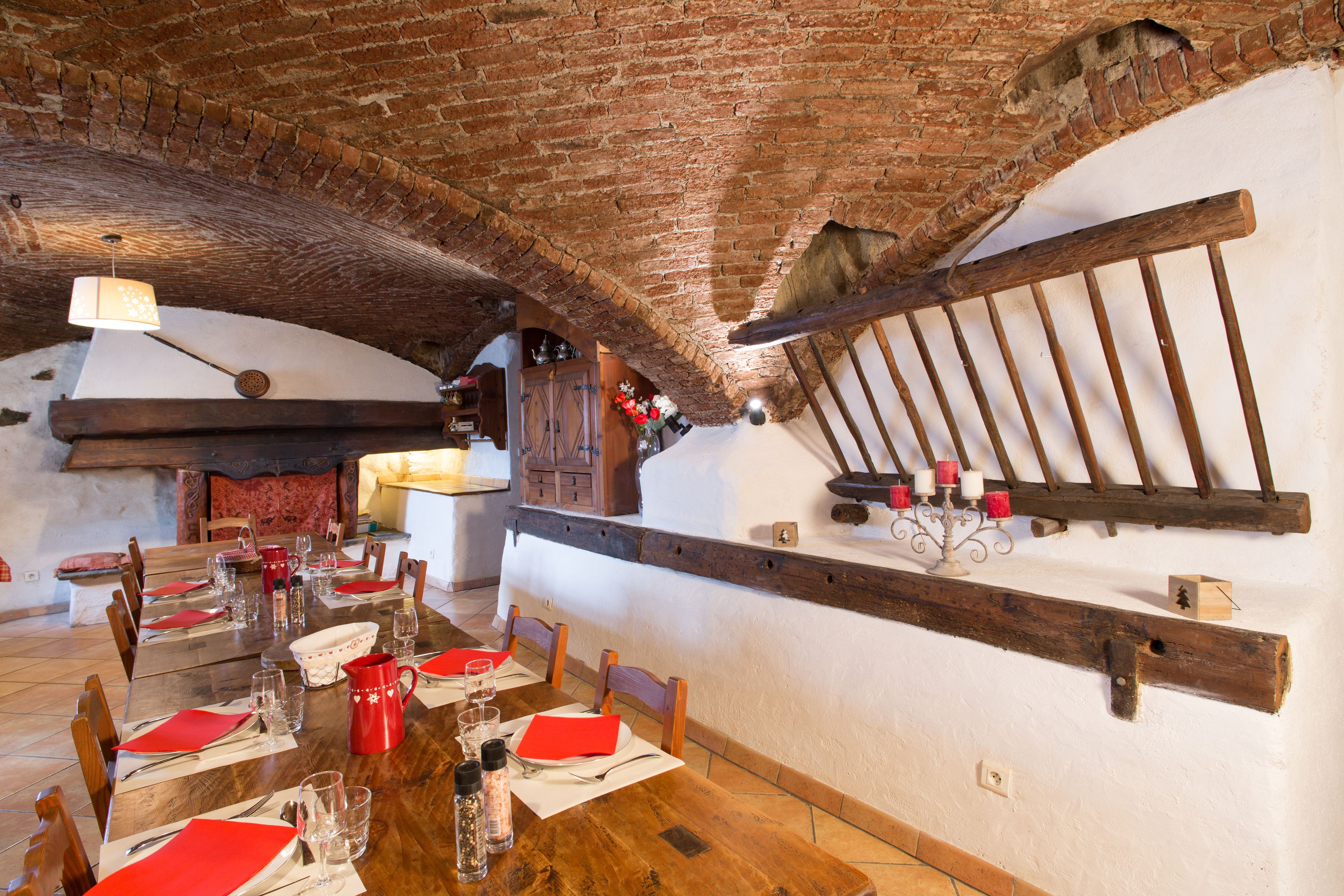 A rustic dining area with a wooden table set for a meal, brick ceiling, and a wooden beam shelf with candles.