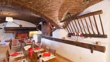 A rustic dining area with a wooden table set for a meal, brick ceiling, and a wooden beam shelf with candles.