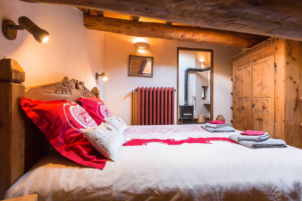 Un dormitorio con cabecera de madera, cama con ropa de cama roja y blanca, un radiador y un armario de madera.
