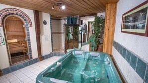 Ein Wellnessbereich mit Whirlpool, Holzboden, gefliesten Wänden und einer Holztür.