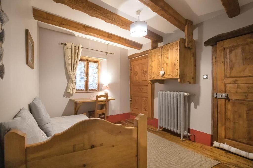 Una habitación con una cama de madera, un escritorio con una lámpara, un radiador y armarios de madera.