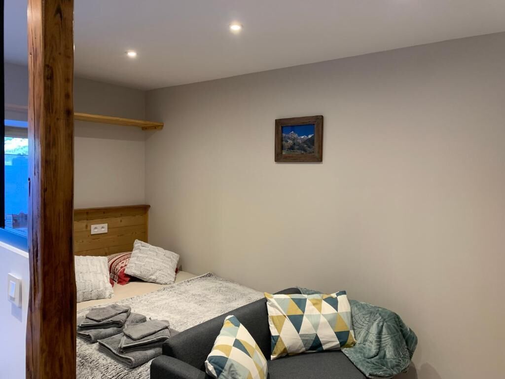 A room with a bed, a sofa, a wooden headboard, a wall-mounted picture, and a window.