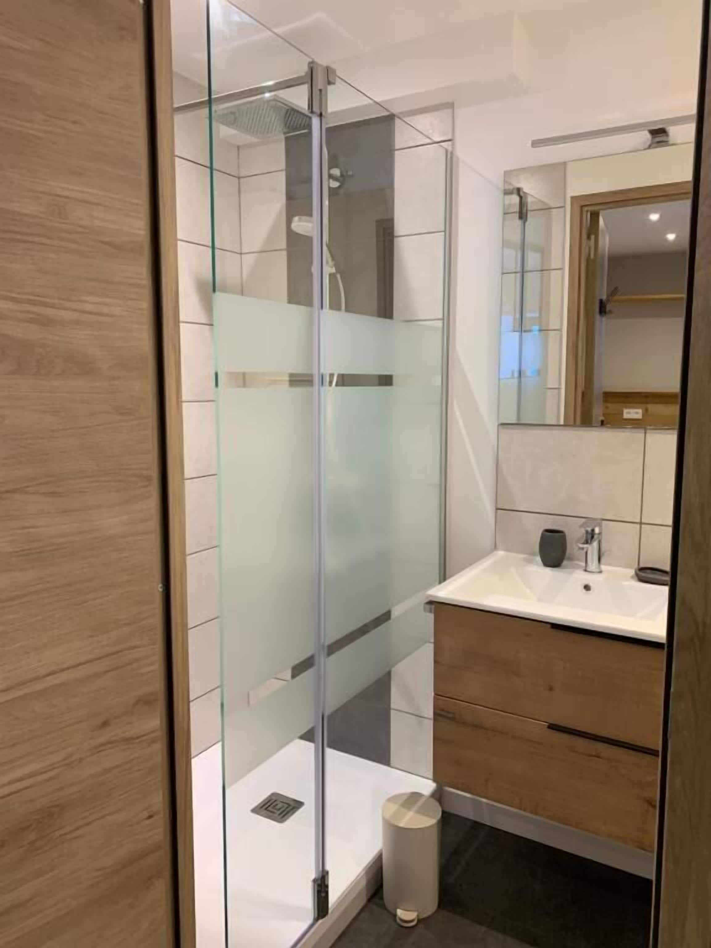 A modern bathroom with a glass-enclosed shower, a white sink, and wooden cabinetry.