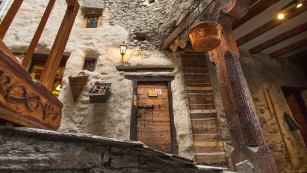 Ein rustikales Steinhaus mit einer Holztür, einer Laterne und einem hängenden Kupfertopf.