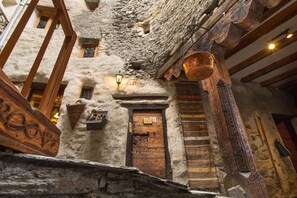 A rustic stone building with a wooden door, a lantern, and a hanging copper pot.