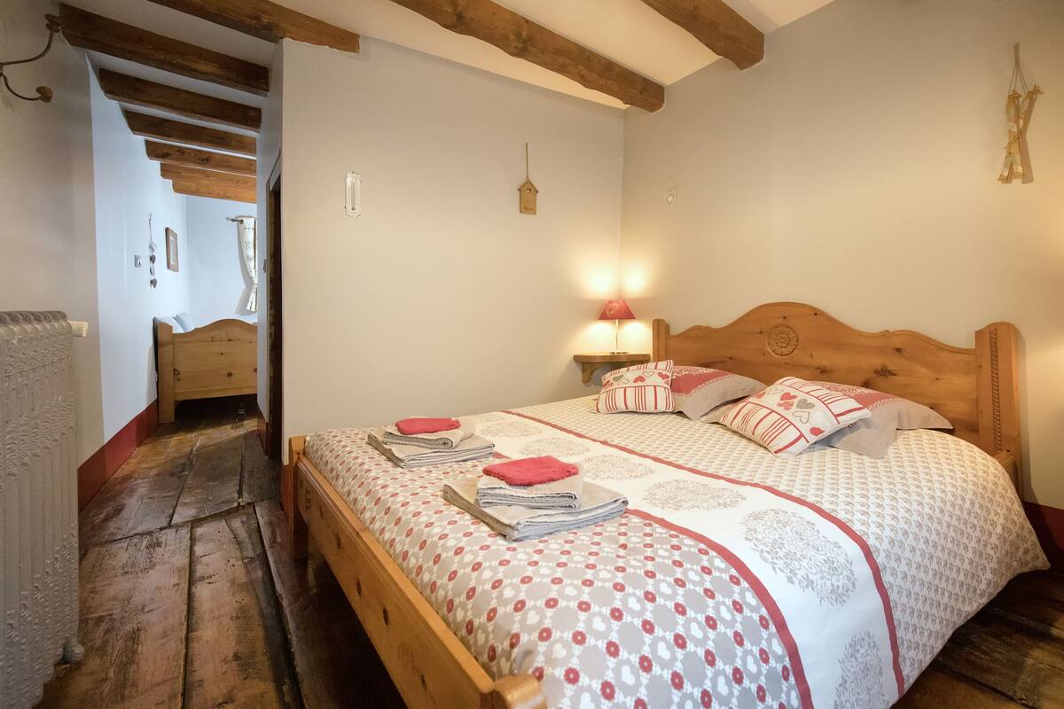 Un dormitorio con cama de madera, una mesita de noche con lámpara y vistas a un pasillo.