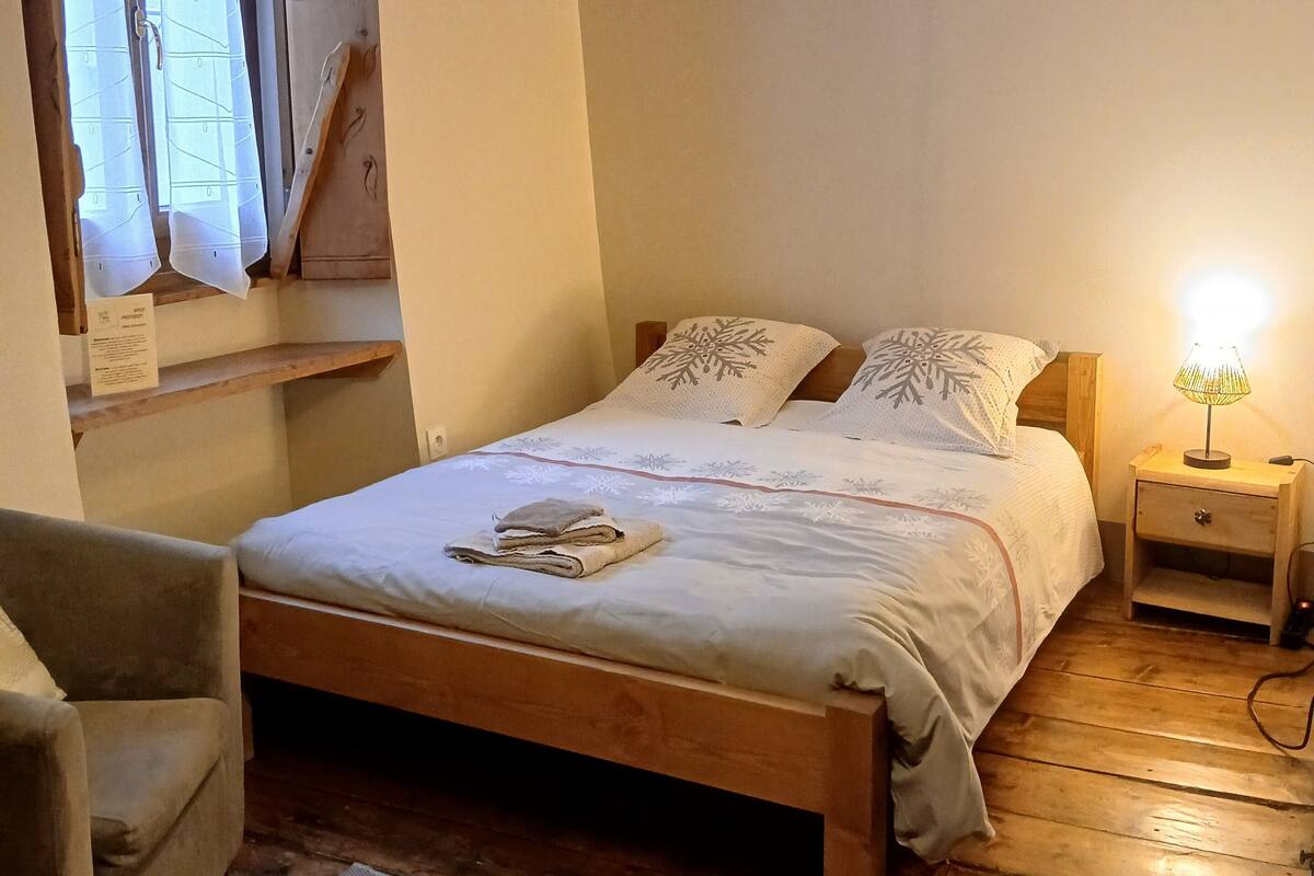 Un dormitorio acogedor con una cama de madera, una mesita de noche, una silla y un ventanal con cortinas.