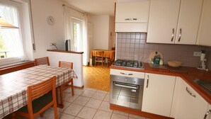 A compact kitchen with a dining area, featuring a stove, oven, and basic cabinetry. - Casa Angelo (Falcade)