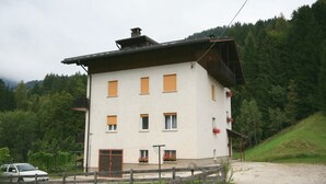A two-story building with a white facade, multiple windows, and a wooden balcony. - Casa Angelo (Falcade)