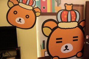 A room with a television on a stand, a door with a push button, and a wall with two cartoon bear decorations. - Fantastic Hostel (Taichung)
