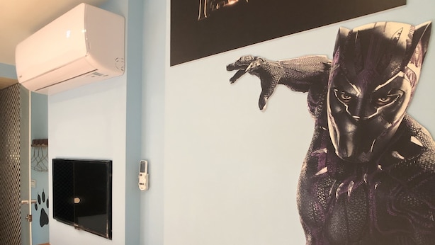 A room with a mounted TV, a wall-mounted air conditioner, and a large poster of a character from a movie. - Fantastic Hostel (Taichung)