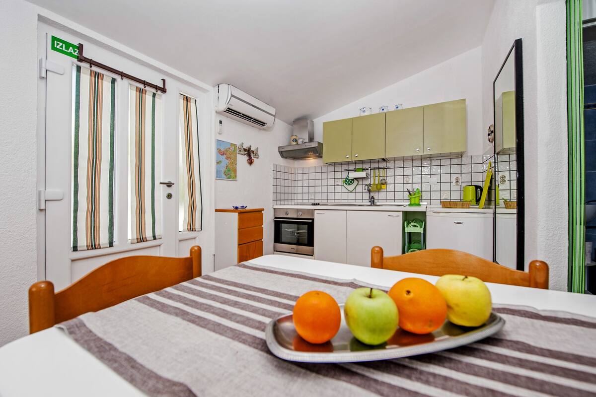 Uma cozinha compacta com uma mesa de jantar, um prato de frutas e uma toalha de mesa listrada.