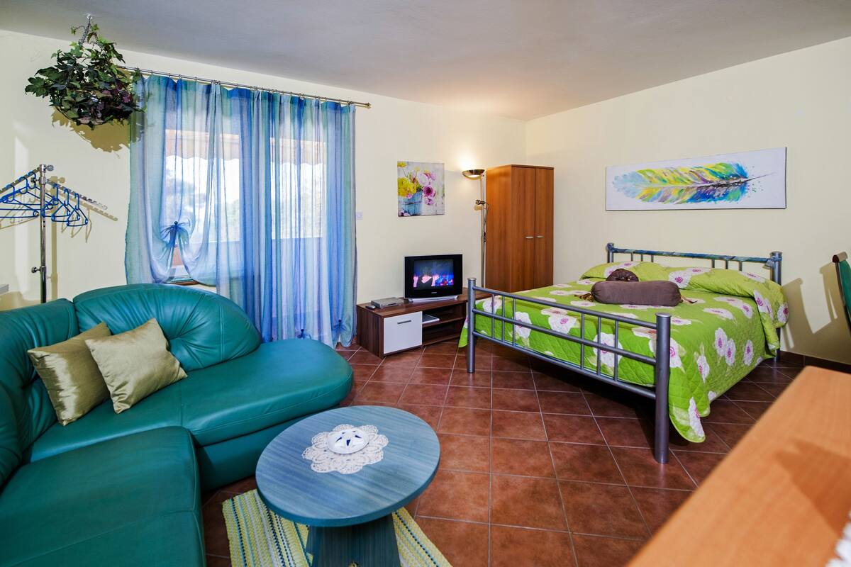 Um quarto com um sofá verde, uma cama com roupa de cama floral, uma televisão e um guarda-roupa de madeira.
