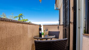 A small outdoor patio with a table and chairs, a striped umbrella, and a bottle of wine.