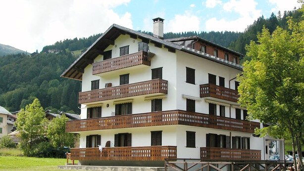 A multi-story building with balconies, surrounded by a grassy area and trees. - Casa Campanula (Falcade)