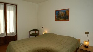 A room with a bed, a chair, a painting on the wall, and a lamp on a bedside table. - Casa Campanula (Falcade)