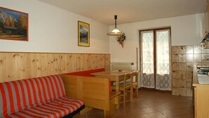 A cozy room with a wooden bench, a striped sofa, a dining table with chairs, and a kitchen area. - Casa Campanula (Falcade)