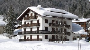 A multi-story chalet with balconies, surrounded by snow-covered trees and mountains. - Casa Campanula (Falcade)