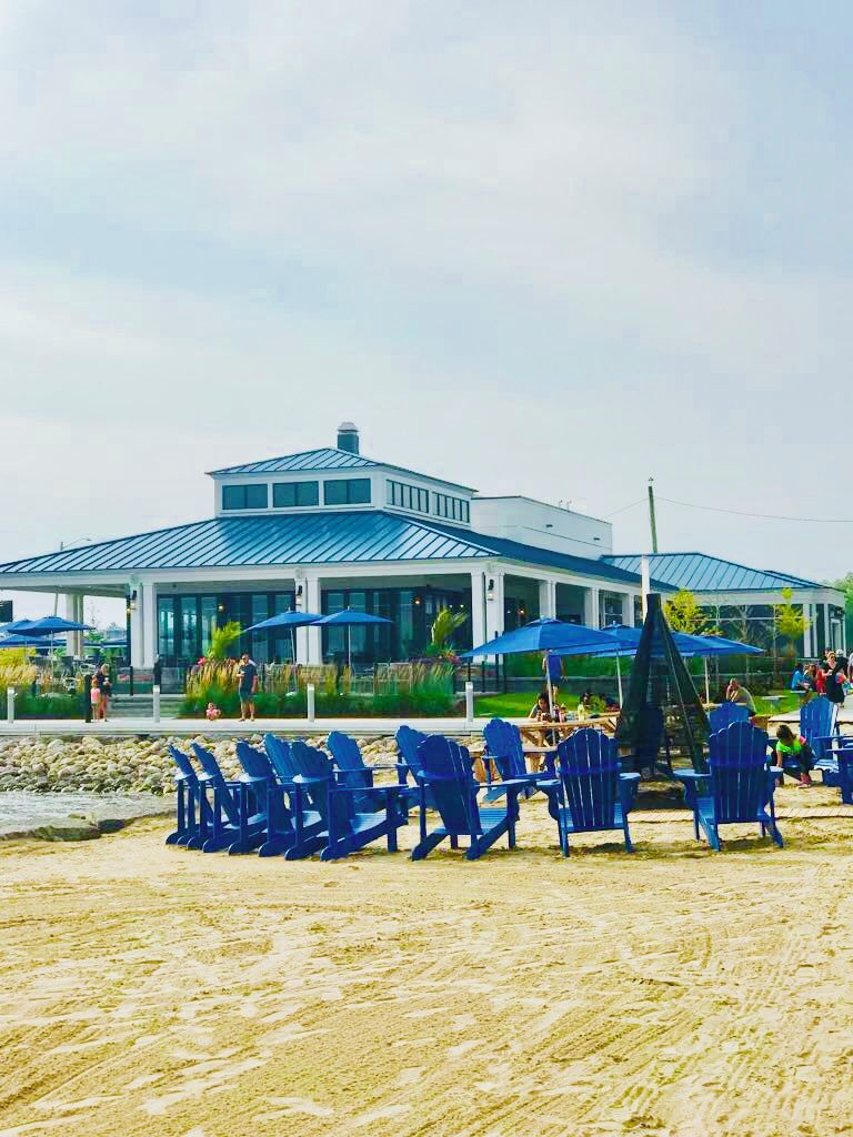 A beachside building with a covered patio area, blue chairs, and umbrellas.