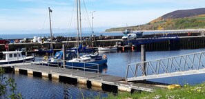 A harbor with boats docked, a pier, and a hilly landscape in the background. - Bannockburn Inn (Helmsdale)