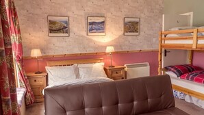 A bedroom with a bed, a bedside table, a lamp, a radiator, and a bunk bed.