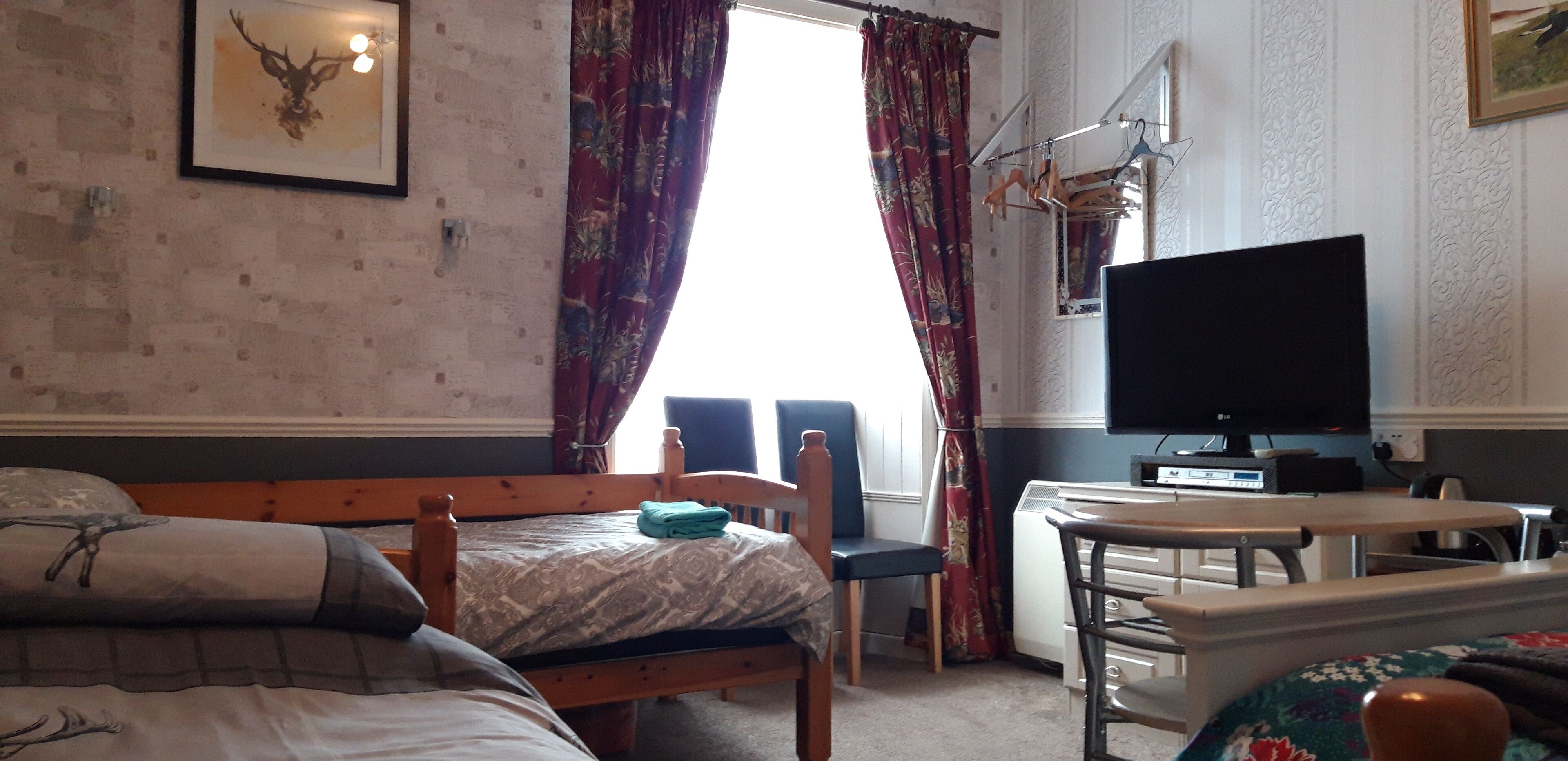 A bedroom with a bed, a desk, a chair, a television, and a window with curtains.