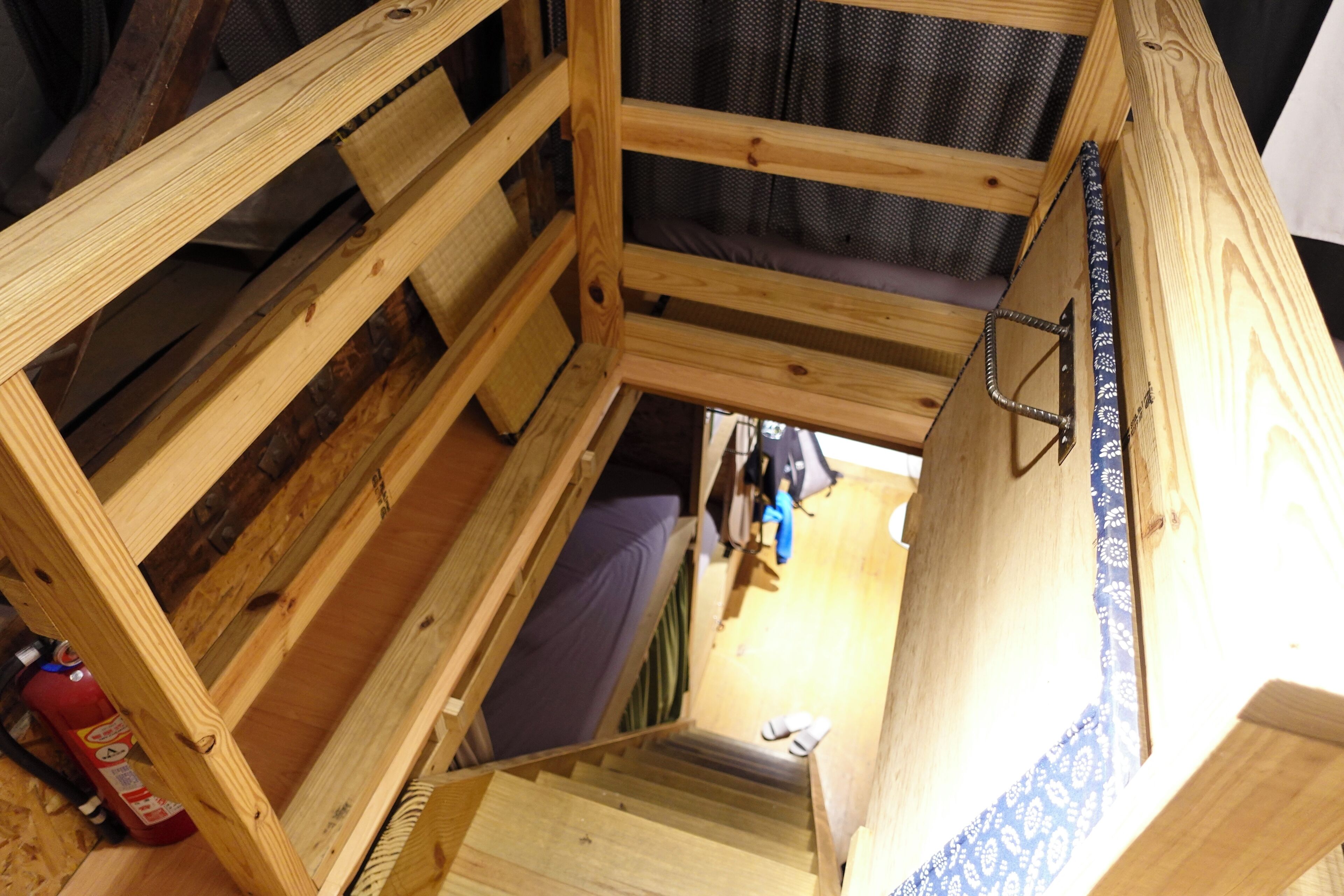 A wooden loft-style room with a bunk bed, a small staircase, and a view of the outside.