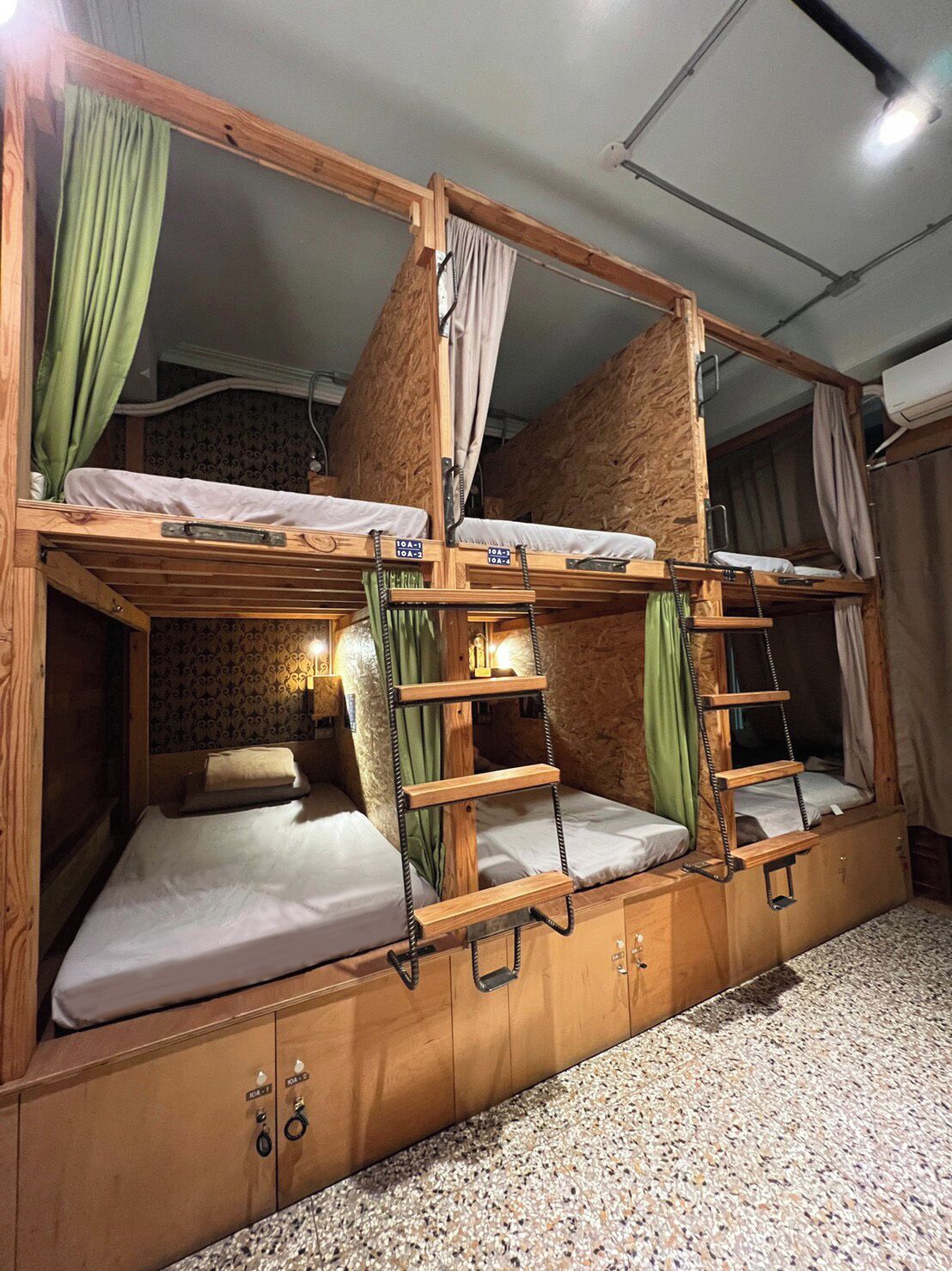 Dormitorio con literas de madera, cortinas verdes y una pequeña estantería.