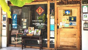 A hostel with a wooden facade, a sign reading 'YUAN QI HOSTEL,' and various informational posters and signs on the glass door. - Yuan Qi Hostel (Tainan)