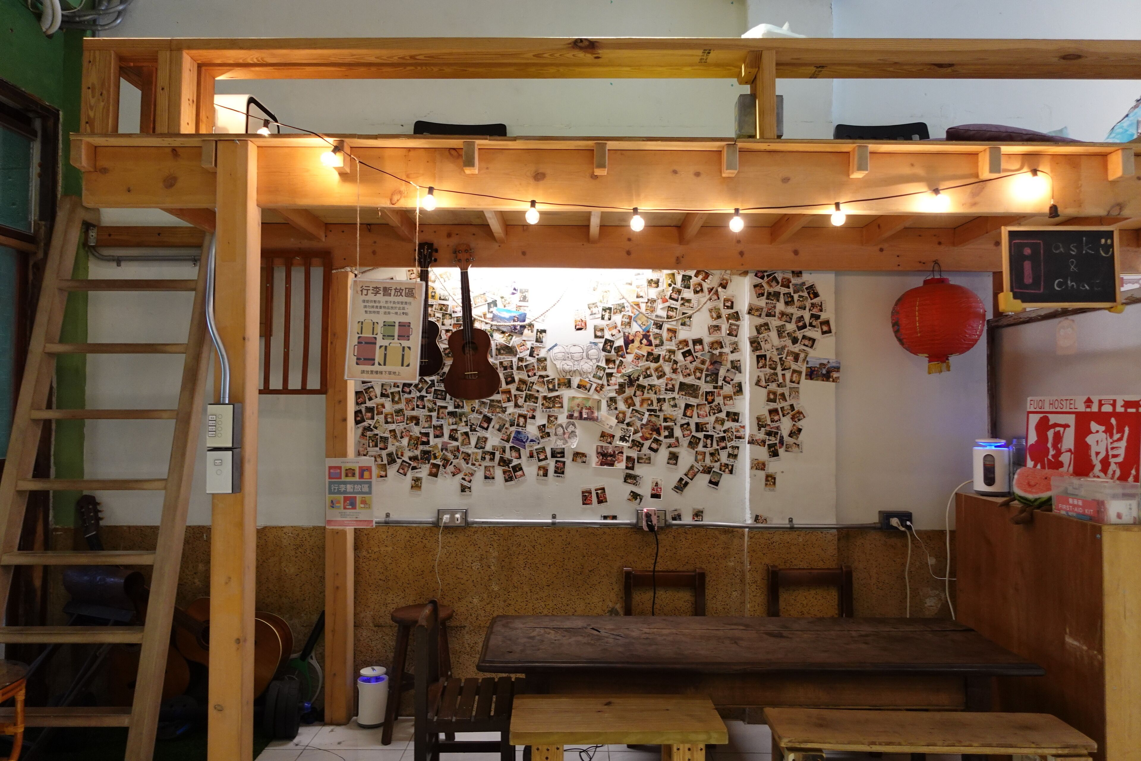 A cozy room with a wooden ceiling, string lights, a guitar, a wall covered with photos, and a chalkboard with writing.