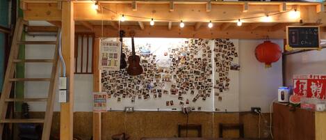 A cozy room with a wooden ceiling, string lights, a guitar, a wall covered with photos, and a chalkboard with writing.