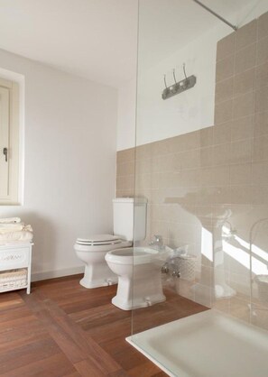Ein Badezimmer mit zwei Toiletten, einer Duschkabine aus Glas und einem weißen Waschbecken.