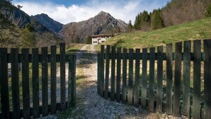 A wooden gate leading to a house with a mountain backdrop.